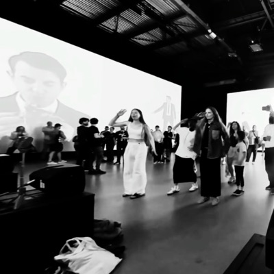 A crowded venue with the work on a large screen
